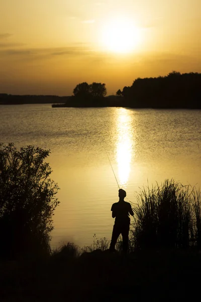 A young man catches fish in the lake at sunset. Beautiful sun re — Stock Photo, Image