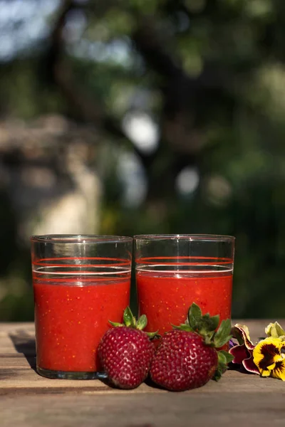 草莓汁和玻璃杯放在木制桌子上 在绿色花园的背景上 放在桌上的是成熟的草莓 有用的食物 文字位置 — 图库照片