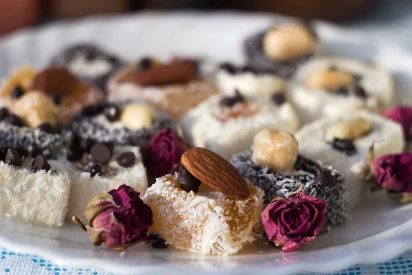 Assorted Turkish delight on a white plate. Traditional yellow, white and black sweets with nuts, dried roses ornaments. Goodies