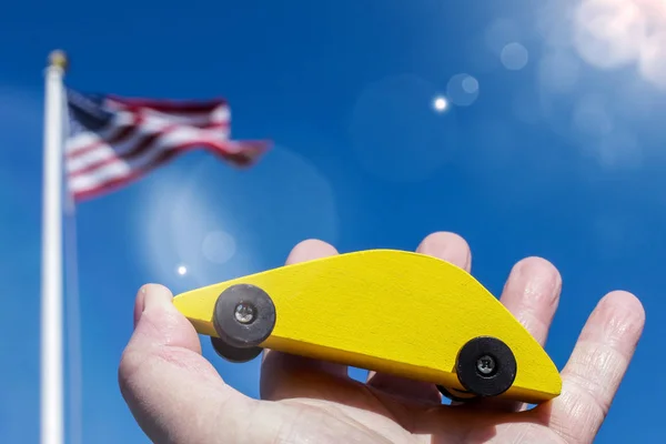 黄色木制汽车举行对蓝天与美国国旗 — 图库照片