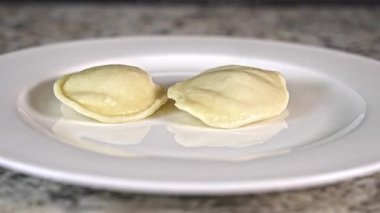 Homemade ravioli added on a white plate. They showcase a perfect shape and texture, inviting a closer look at their smooth surface and subtle shine. Ideal for a cozy meal.