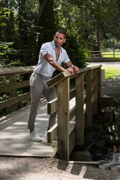 夏の服の黒い肌の男は木製の橋の上に立っている 晴れた日 ハンサムな男の肖像画 — ストック写真