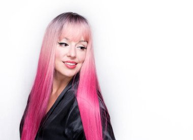 Uzun pembe saçlı beyaz bir kadın, ipek ev bornozu giyiyor, yan bakıyor, gülümsüyor, gri arka planda soyutlanmış.