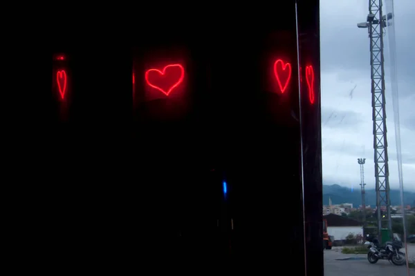 Neon light bright red heart reflections on the transparent plastic screen