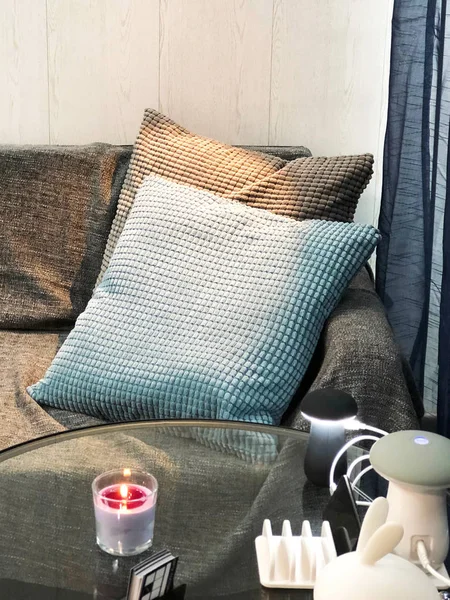 Two pillows on the sofa as waiting zone in studio with candle, phone chargers and lamp