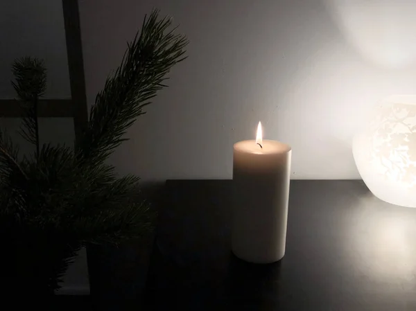 Burning white candle on black table with green fir tree and flower ornament lamp