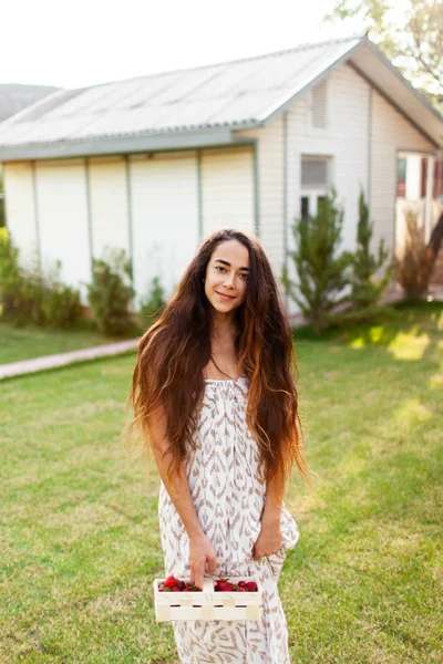 Beautiful girl with long hair enjoying summer day in a country house and eats strawberries. unity with nature. The woman inhales fresh air. The woman enjoys living.