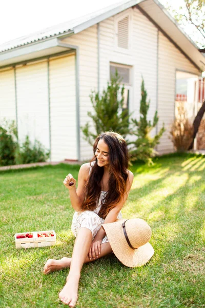 Beautiful girl with long hair enjoying summer day in a country house and eats strawberries. unity with nature. The woman inhales fresh air. The woman enjoys living.