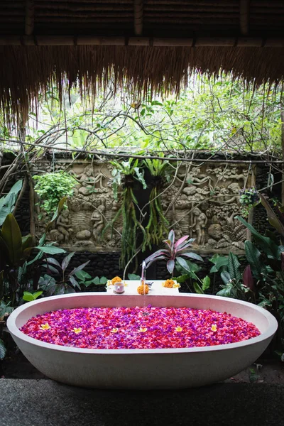 高級ホテルのバスルームと赤とピンクの熱帯花 熱帯の花びらを持つスパ概念バスタブ 自分のための時間 — ストック写真