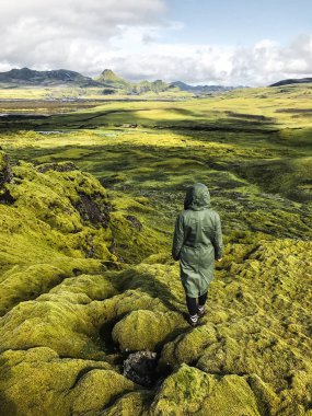 Yosun görünümünü genç kadının huzurlu meadows İzlanda'daki kaplı. Kuzey Kutup Dairesi vahşi doğa. İnsanlar ve doğa bağlantı. Rahat su geçirmez yeşil parka giyen erkek