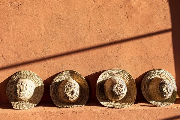 Солом'яні пляжні капелюхи стоять на теракотовій глиняній стіні. Яскраве сонячне світло — стокове фото