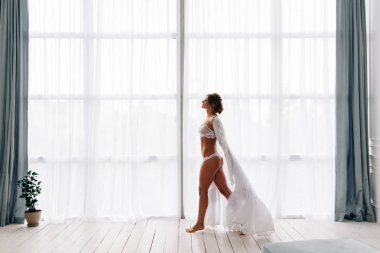 Pencerenin kenarında gelinlik, ipek elbise ayakta onu lüks yürüyüş güzel mutlu gelin.