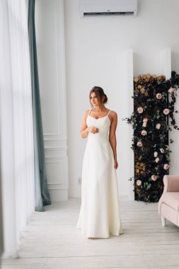 Düğün. Gelin beyaz studio iç gibi evde oturup güzel elbiseli. Moda düğün tarzı tam uzunlukta vurdu. Genç çekici beyaz sarışın model bir gelin gibi