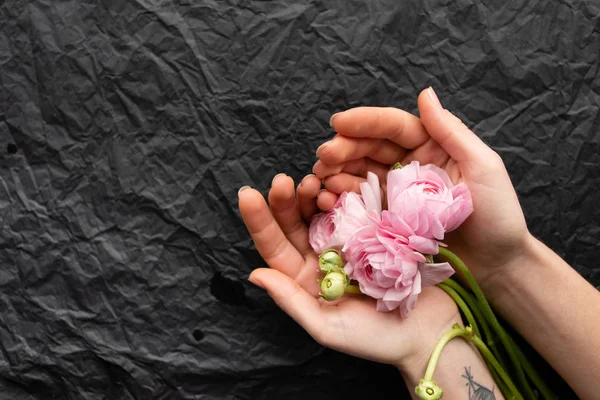 Three tender peonies in the hands of a tender girl. Black rumpled background.