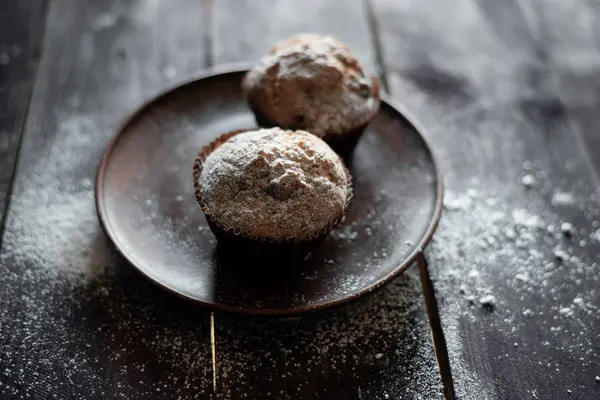 Dois muffins de chocolate em uma mesa de madeira, polvilhados com açúcar doce — Fotografia de Stock
