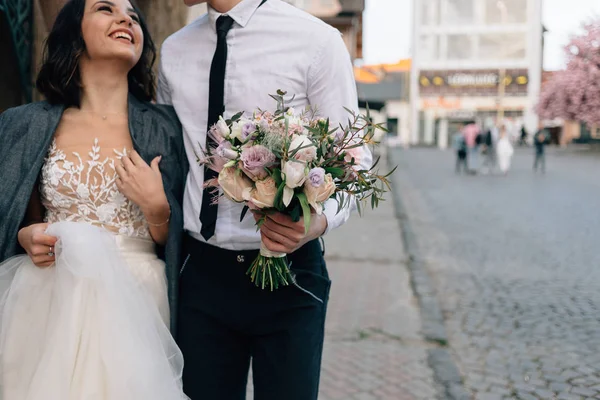Bruiloft boeket in de handen van de bruidegom. Bruid en bruidegom lopen langs de straat — Stockfoto