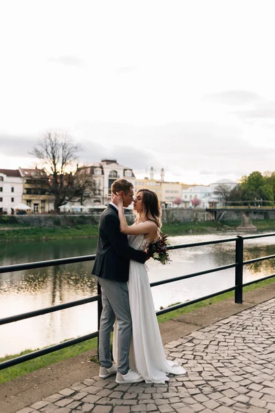 Наречений і наречений щасливі і смішні в день весілля йдуть вздовж набережної біля річки — стокове фото