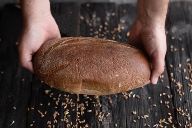 iki el koyu bir arka plan üzerinde koyu çavdar ekmeği bir somun tutun