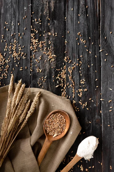 Een houten tafel op het zijn lepels in hen tarwe, meel, in de buurt van de oren van tarwe — Stockfoto