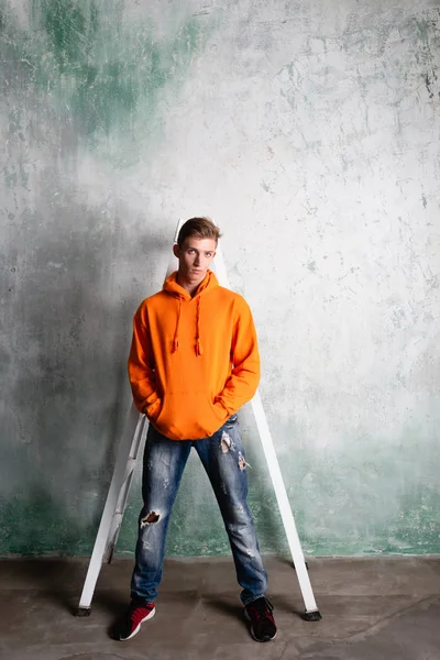 Bir inşaatçı ellerini cebinde tutarak bir merdivenin yanında duruyor Stok Fotoğraf
