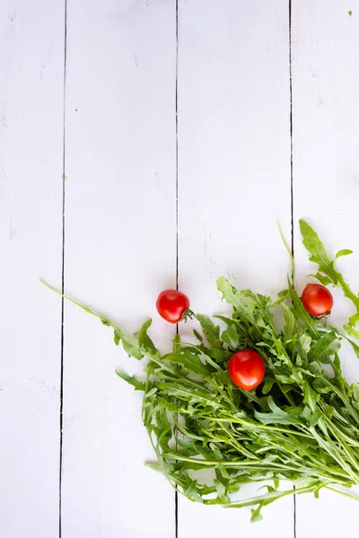 Arugula leaves and cherry tomatoes lie on a kitchen table made of wood — Stock Photo, Image