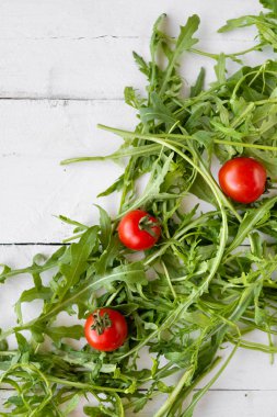 Roket salatası masada bırakır. Onlar yeşil ve mouthwatering, kırmızı kiraz domates yakın.