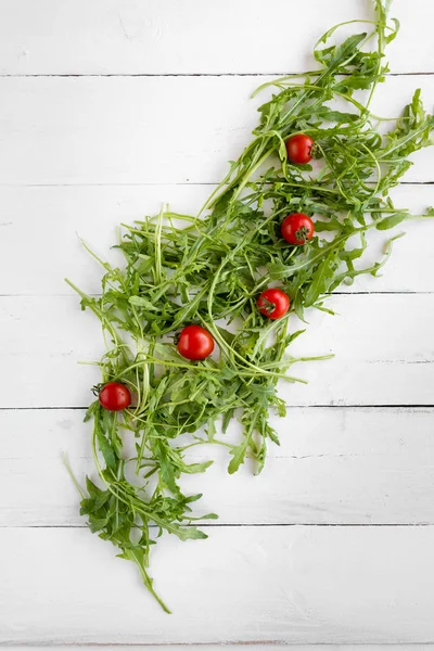 Salata yapraklı arugula için malzemeler ahşap bir masaya yayılmış. Onlarla serin küçük domates vardır — Stok fotoğraf