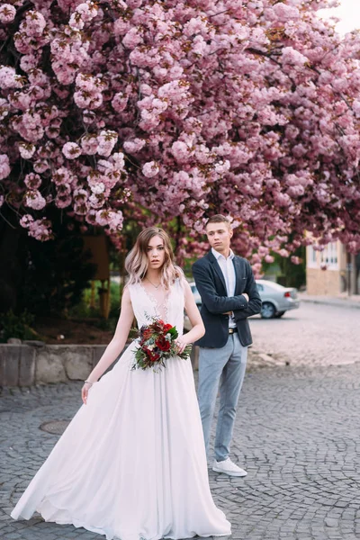 Milující manželská nevěsta a ženich oblečená do styulnaya oblečení u stromu v čerstvém vzduchu — Stock fotografie