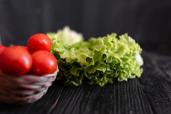 Hele en rijpe tomaten liggen op de tafel bij de bladeren van sla — Stockfoto