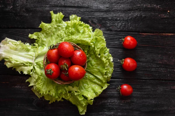 Een nieuw gewas van groenten op de keuken tafel, rijpe en sappige tomaten liggen op de bladeren van groene salade — Stockfoto