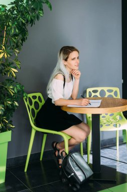 bir kafede oturan pensive öğrenci bir dergide bir sandalyede oturan bir kompozisyon yazma hazırlanıyor