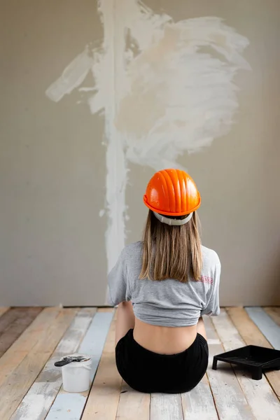 Naprawa domu, zespół budowlany, dziewczyna siedzi na drewnianej podłodze i patrzy na ścianę — Zdjęcie stockowe