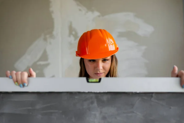 Kobieta w pomarańczowym hełmie budowlanym mierzy równomierność — Zdjęcie stockowe