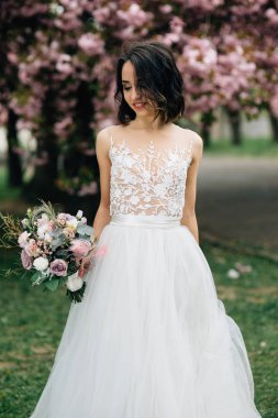 parkta sevimli gelinin düğün yürüyüşü, çiçek bir buket ile gelinlik kız