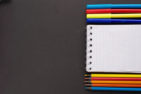 Preparación para dibujar en el cuaderno de bocetos. cuidadosamente dispuestos lápices marcadores y un cuaderno sobre un fondo negro . — Foto de Stock