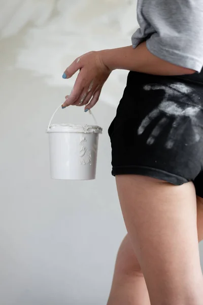 Uma foto de close-up de uma menina suja com massa branca segurando um balde contra um fundo de paredes de gesso . — Fotografia de Stock