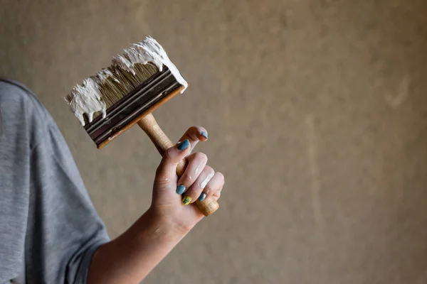 Foto de cerca de la parte del cuerpo de una chica, una mano sostiene un pincel de construcción manchado de pintura . — Foto de Stock