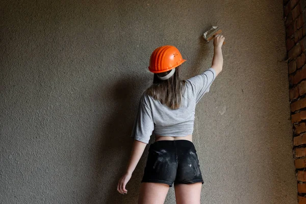 Budowniczy dziewczyna ma na sobie czarne szorty i szary T-shirt ochronny pomarańczowy kask. — Zdjęcie stockowe