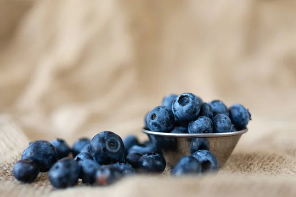 Fresh organic blueberries in a plate of metal on burlap cloth on a rustic wooden table. — Stock Photo, Image