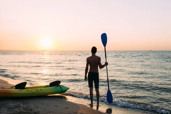 Sziluettje egy fiatal jóképű fickó állt a strandon az óceán tartó lapát a kezében — Stock Fotó