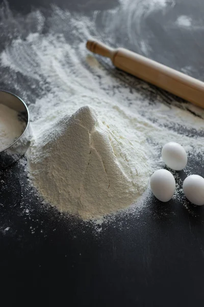 Ingredients for making bread, flour and eggs lie on a black background — Stock Photo, Image