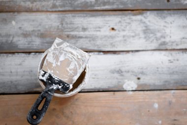 eski ahşap masada beyaz macun ve bir boya fırçası için bir spatulap ile bir kova var.