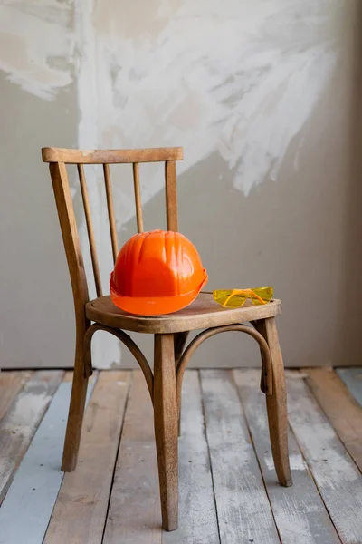 Sur la table en bois est un casque de construction orange et des lunettes de sécurité jaunes . — Photo