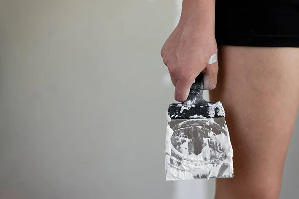 A closeup photo of a girl in her hand holding a construction spatula smeared into white putty.