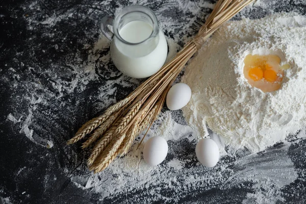 A mountain of flour, an egg yolk in it, next to it is a wheat of spikelets and a jug of milk — Stock Photo, Image