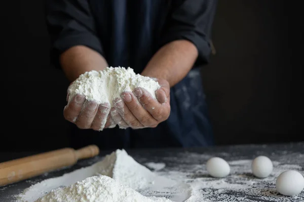male chef, male hands are holding a big handful of flour on a black background.