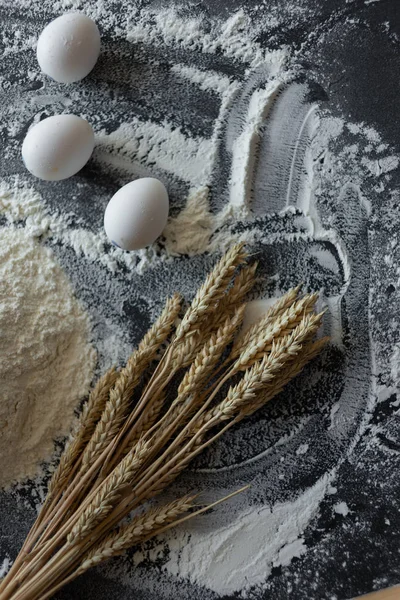 Tre uova di pollo su fondo nero, farina di frumento e spighe di cereali . — Foto Stock