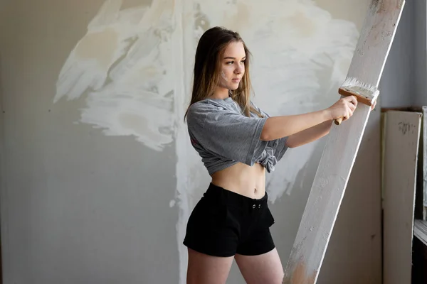 A young girl designer updates the interior paints the walls and boards in white. — Stock Photo, Image
