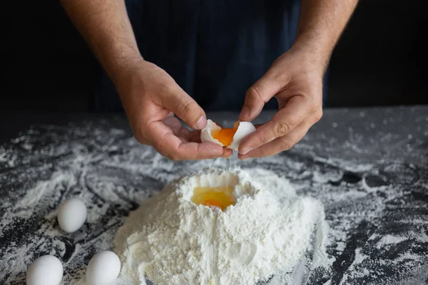 male chef in the kitchen, hands smashed a chicken egg over a pile of flour