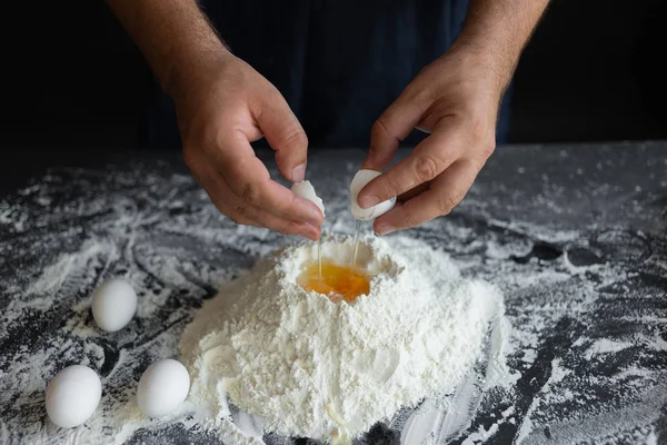 Impasto di cottura, mani maschili rompere le uova su un mucchio di farina — Foto Stock